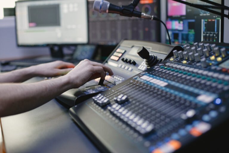 : Hands operating a professional audio mixing console and joystick controller in a broadcast studio, representing live production management and technical consultancy.